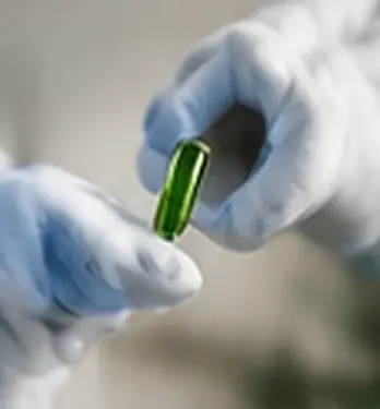 A gloved hand holding a green capsule